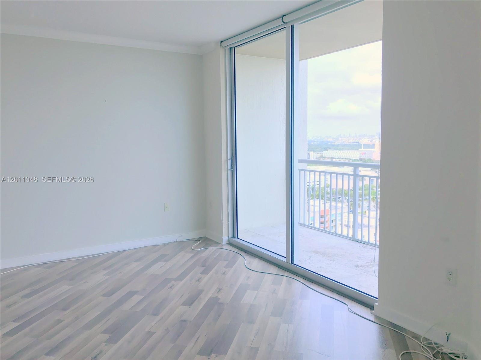 An empty room features light wood-look flooring, white walls, and a sliding glass door to a balcony — 9055 SW 73rd Ct # 1903, Miami FL 33156, MIAMI, FL