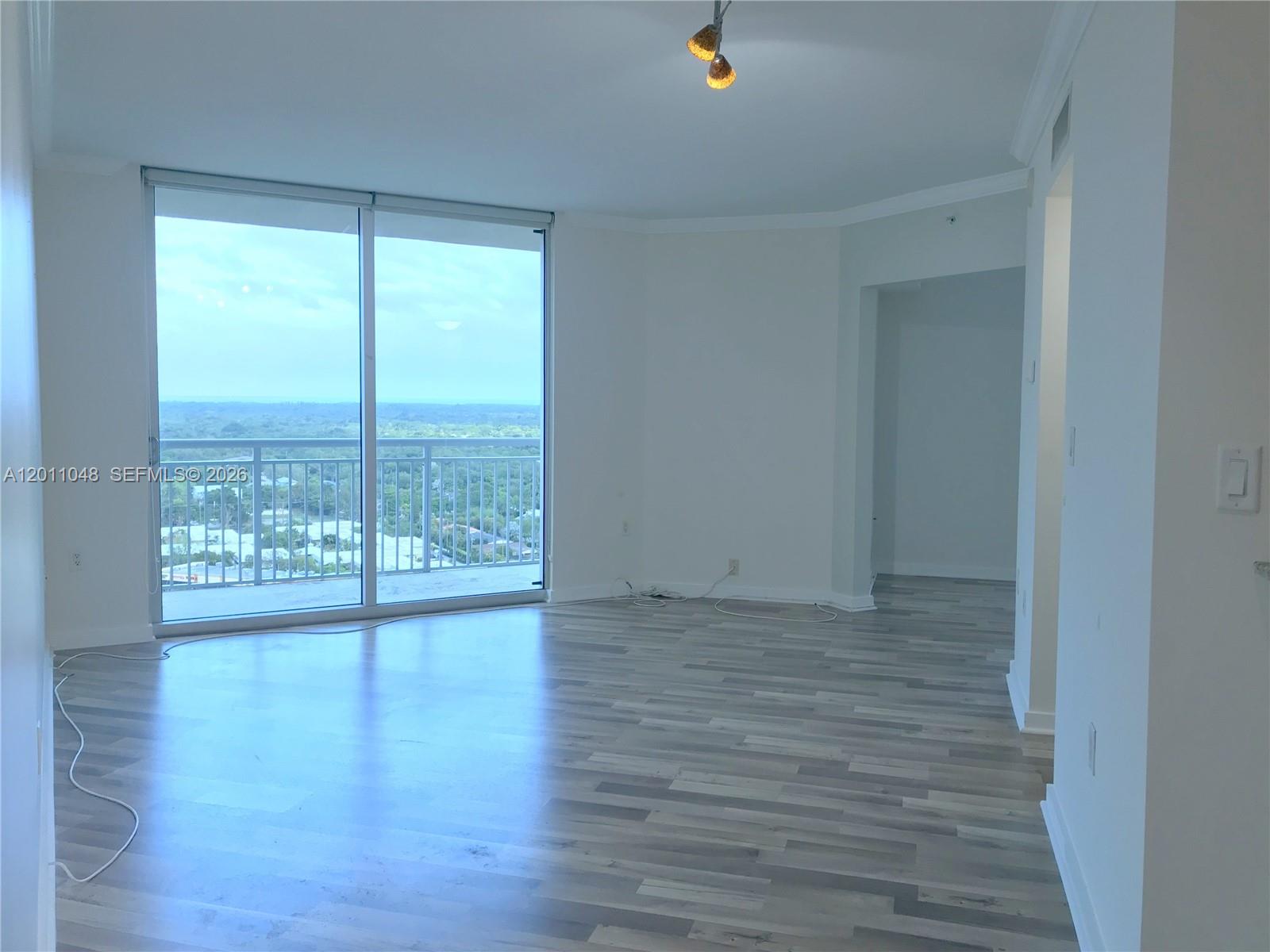 An empty living room features light wood-look flooring, white walls, and a large sliding glass door — 9055 SW 73rd Ct # 1903, Miami FL 33156, MIAMI, FL