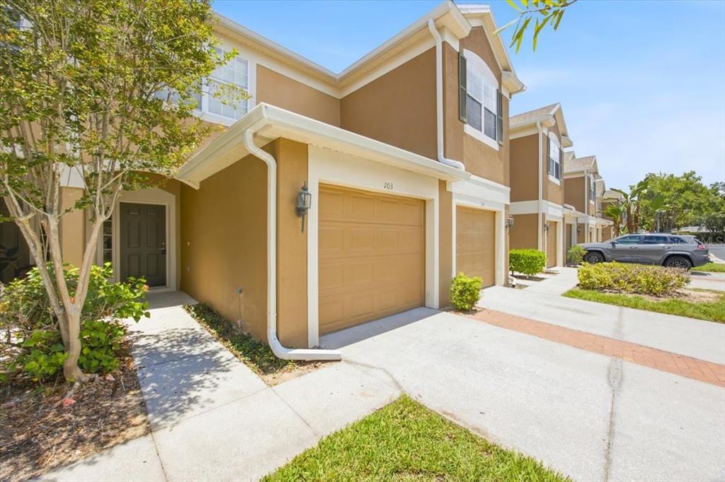 A tan two-story townhouse exterior features a single-car garage and a paved driveway — 6388 CASTELVEN DRIVE UNIT 103, ORLANDO, FL