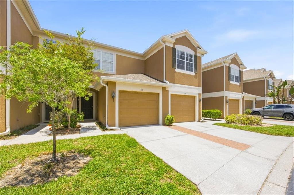 A row of two-story townhomes with tan stucco siding, attached garages, and concrete driveways — 6388 CASTELVEN DRIVE UNIT 103, ORLANDO, FL