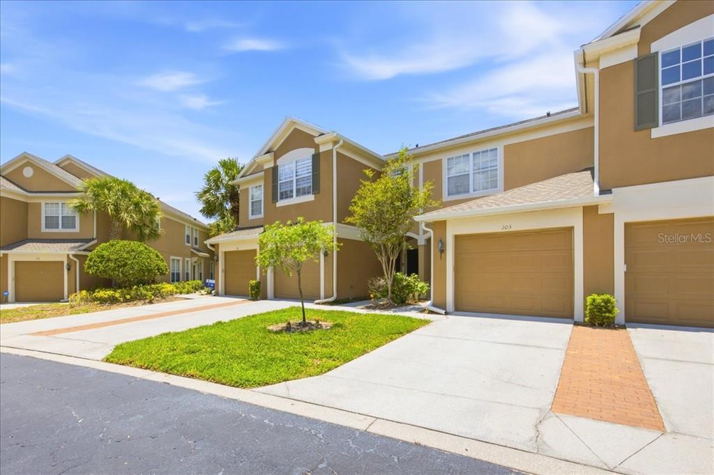 A row of tan townhouses with attached garages and concrete driveways under a blue sky — 6388 CASTELVEN DRIVE UNIT 103, ORLANDO, FL