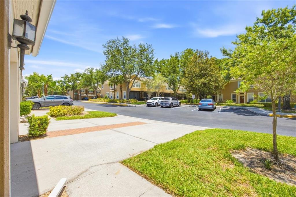A view from a sidewalk looking toward a parking lot with cars and apartment buildings — 6388 CASTELVEN DRIVE UNIT 103, ORLANDO, FL