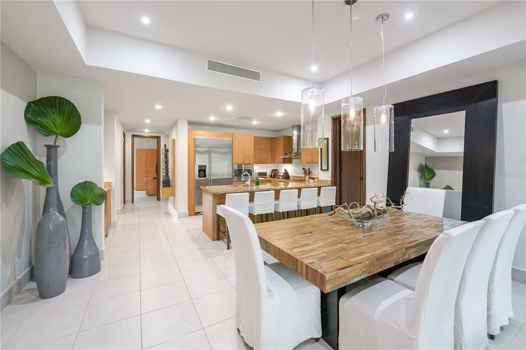 A dining area with a wooden table and white chairs opens into a modern kitchen — Bahia Beach Golf Club LAS VERANDAS CONDOMINIUM UNIT 5134, RIO GRANDE, PR