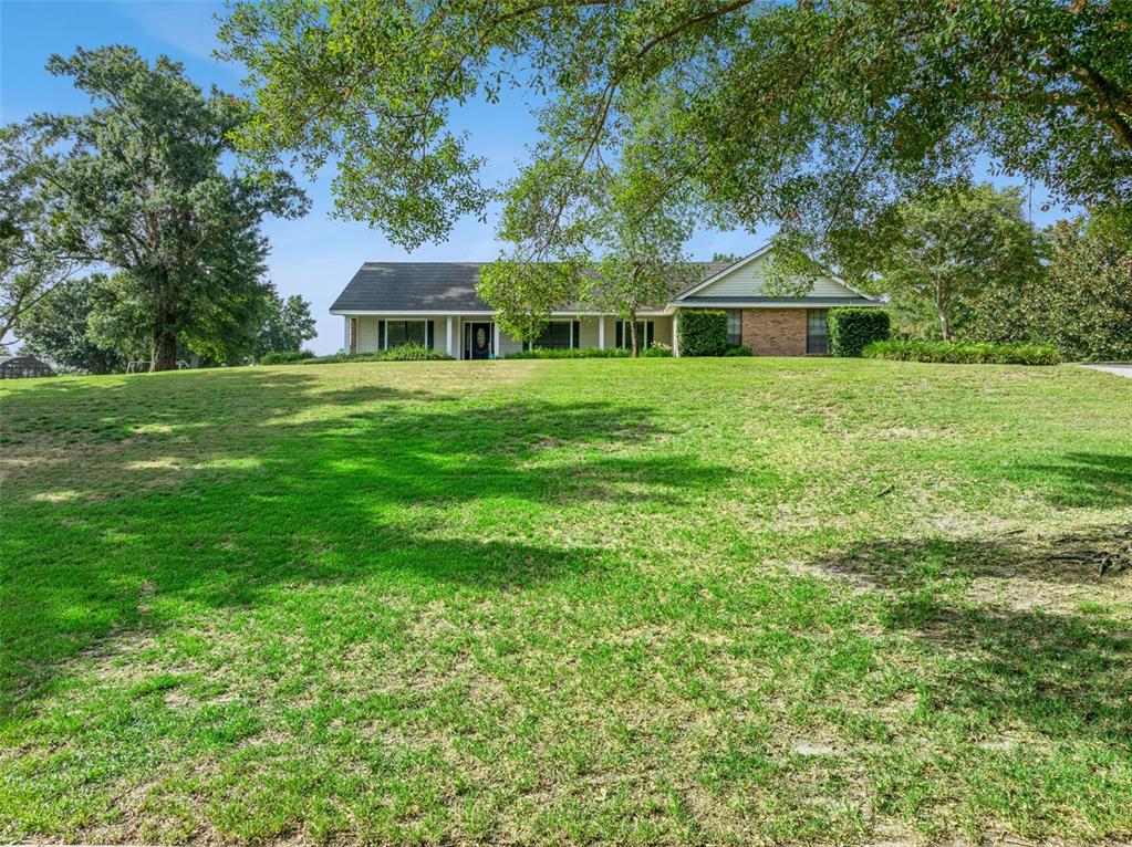 A single-story house with a brick and siding exterior sits atop a large grassy hill — 9225 MCDAVID COURT, WINDERMERE, FL