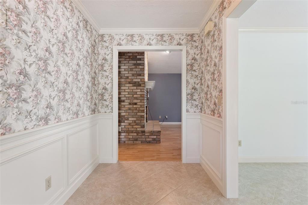 A tiled entryway features floral wallpaper above white wainscoting, leading to a room with brick fireplace — 9225 MCDAVID COURT, WINDERMERE, FL
