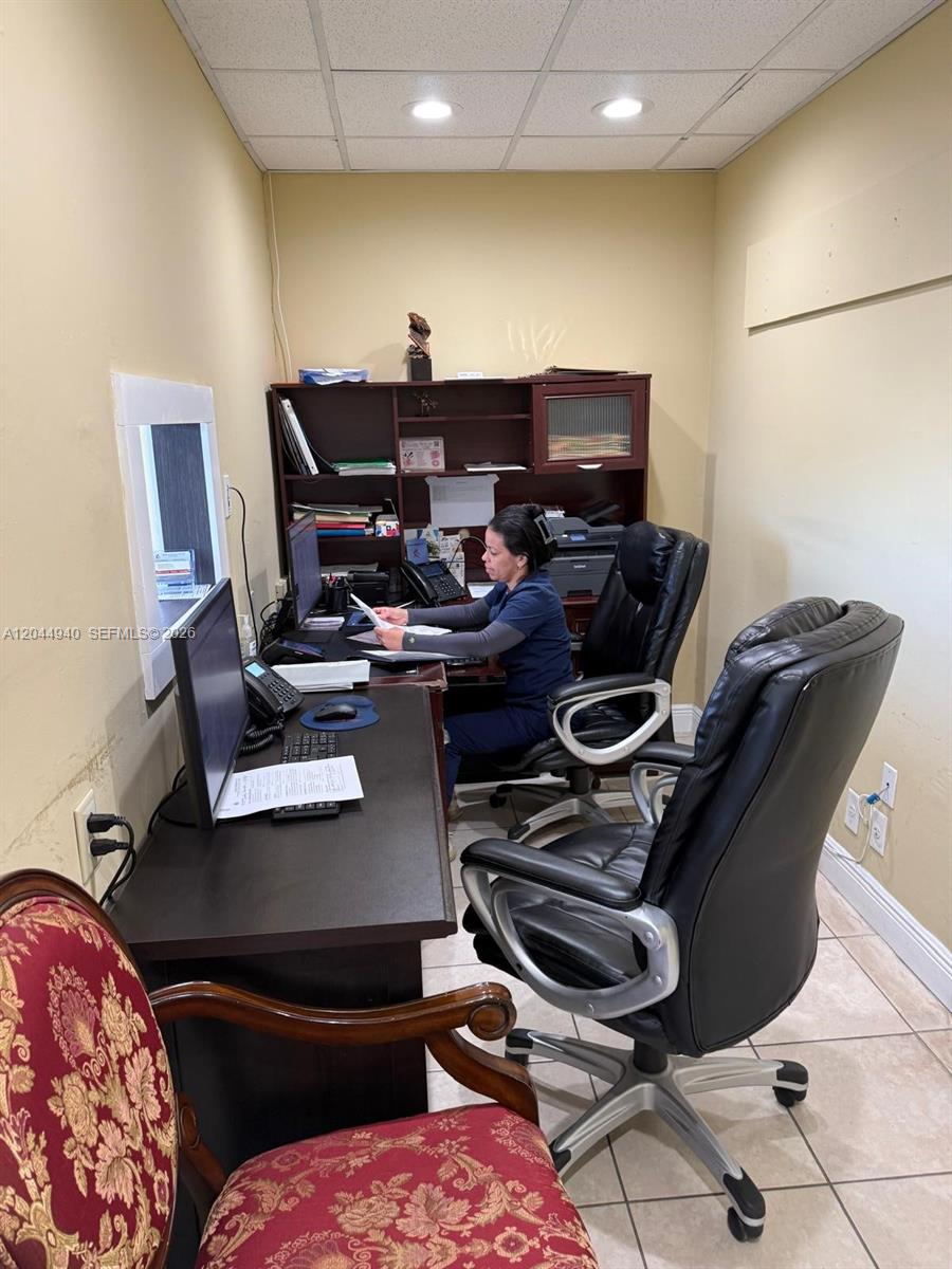 A woman sits at a desk in a small office with tan walls and tile floors — 3700 W 12th Ave Suite 3762, Hialeah FL 33012, HIALEAH, FL
