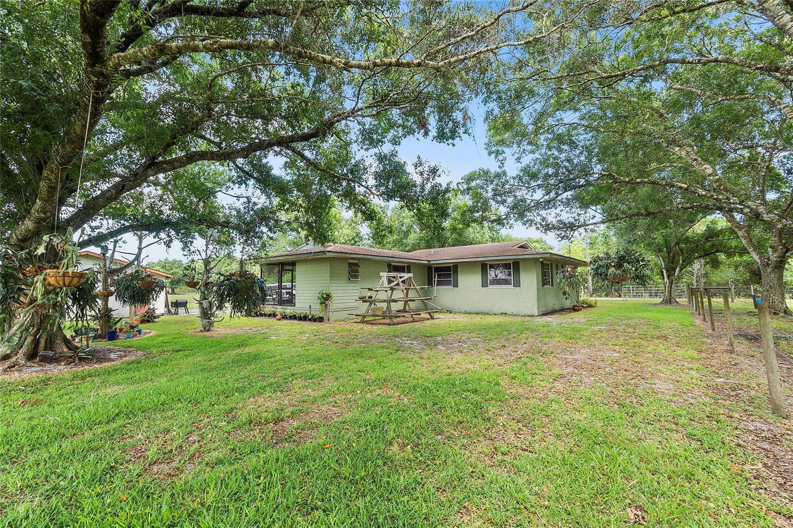 A light green single-story house sits on a grassy lot shaded by large oak trees — 10120 W Midway Road, Fort Pierce FL 34945, FORT PIERCE, FL