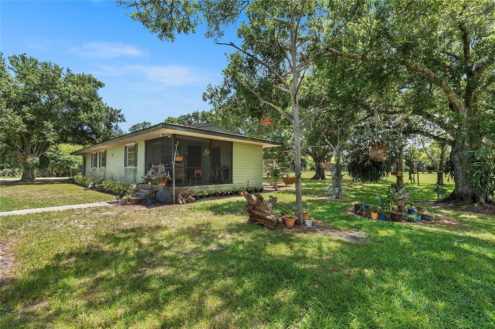A light green house with a screened-in porch sits on a grassy lot with trees — 10120 W Midway Road, Fort Pierce FL 34945, FORT PIERCE, FL