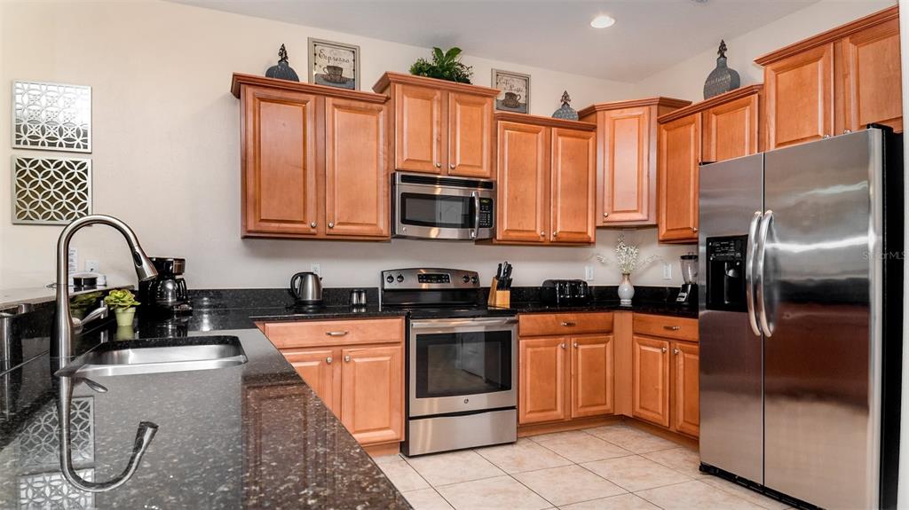 A kitchen features light wood cabinets, dark granite countertops, and stainless steel appliances — 1506 MOON VALLEY DRIVE, DAVENPORT, FL