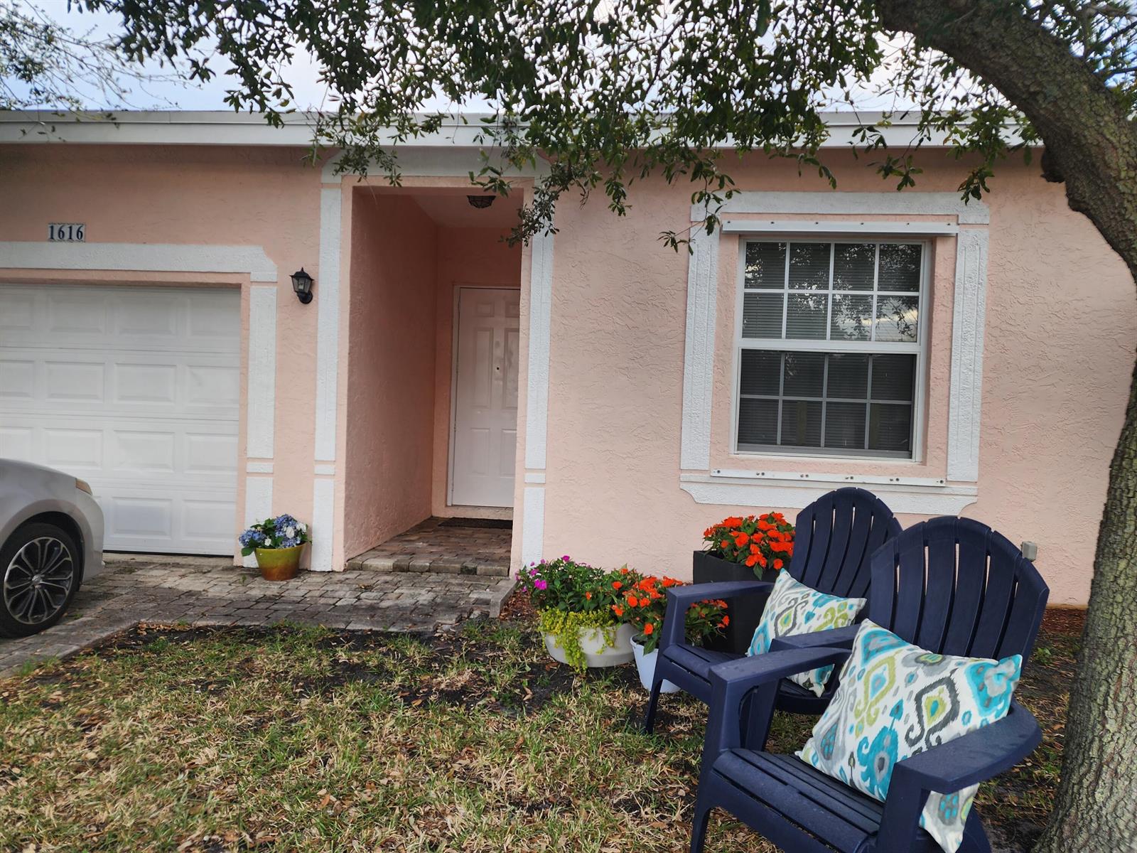 A pink stucco house exterior features a white garage door, front door, and two blue chairs — 1616 S Johnson Street, FL 33460, FL