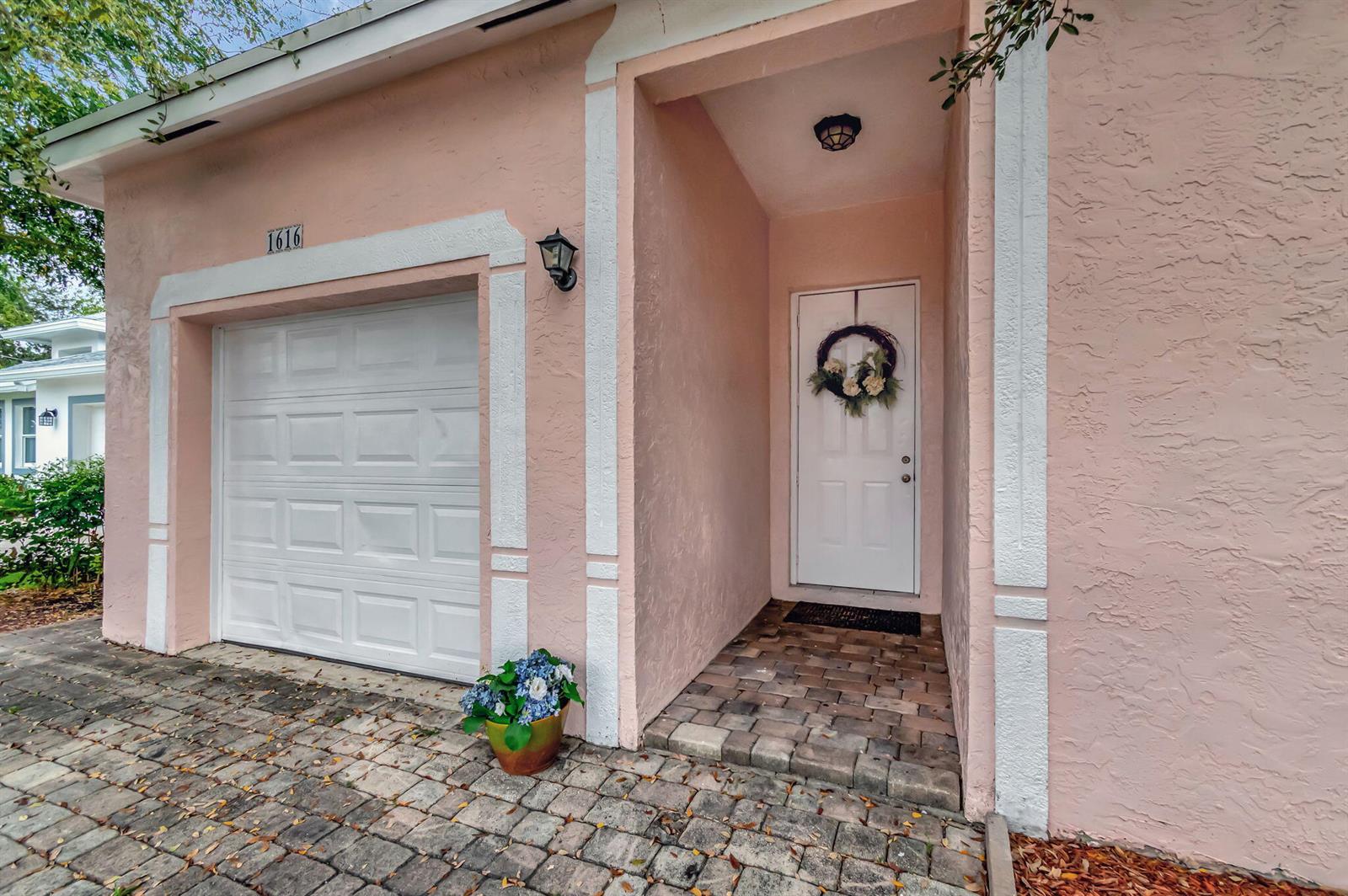 A pink stucco house exterior features a white garage door, a front door, and pavers — 1616 S Johnson Street, FL 33460, FL