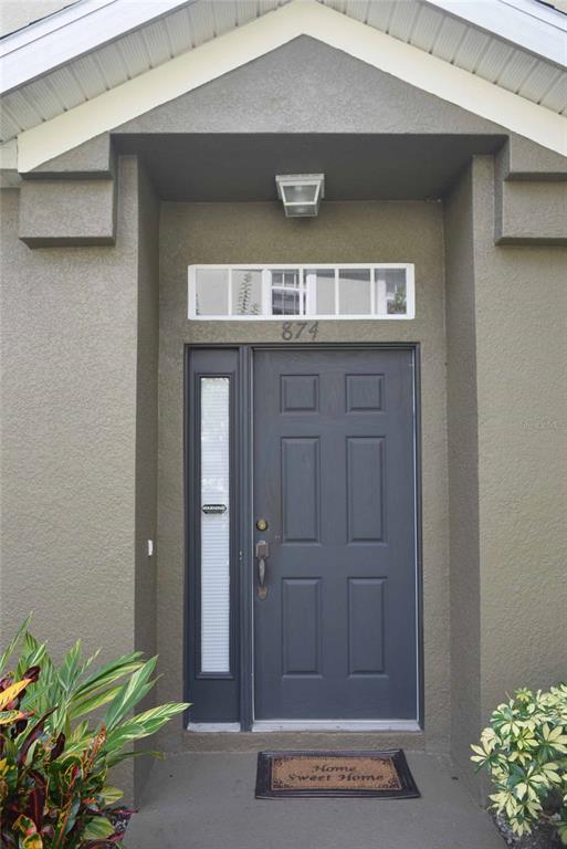 A dark gray front door with a side light and transom window under a porch — 874 ASHWORTH OVERLOOK DRIVE, APOPKA, FL