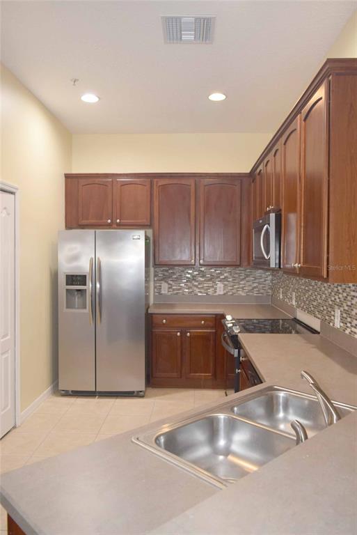 A kitchen features dark wood cabinets, stainless steel appliances, a double sink, and tiled backsplash — 874 ASHWORTH OVERLOOK DRIVE, APOPKA, FL