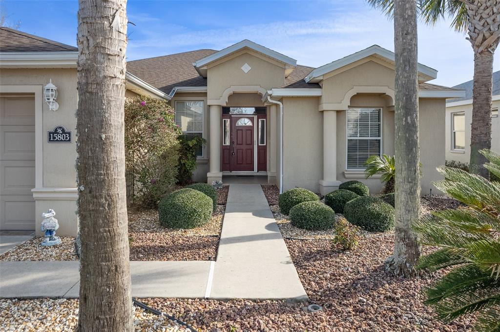 The exterior of a beige single-story house features a red front door and palm trees — 15803 SW 11TH COURT ROAD, OCALA, FL