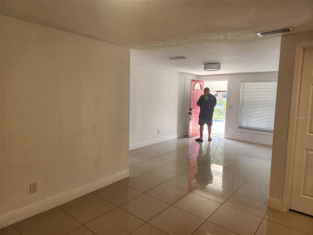 A room with light-colored walls and tiled flooring leads to an open exterior doorway — 8518 WOODLAKE DRIVE, TAMPA, FL
