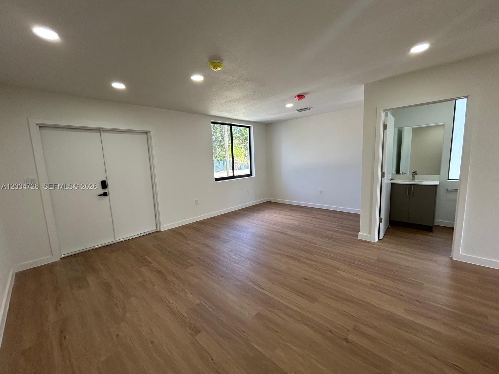 An empty room with light wood-look flooring, white walls, recessed lighting, and an attached bathroom — 19426 SW 125th Ave # 0, Miami FL 33177, MIAMI, FL