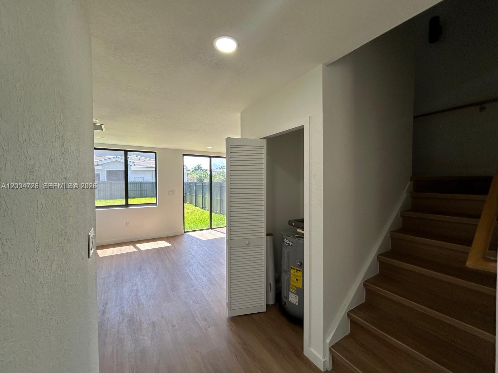A room with wood-look flooring features a water heater closet and stairs leading upward — 19426 SW 125th Ave # 0, Miami FL 33177, MIAMI, FL