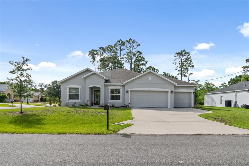 A single-story house with a gray stucco exterior, a three-car garage, and a concrete driveway — 5 BUD HOLLOW DRIVE, PALM COAST, FL
