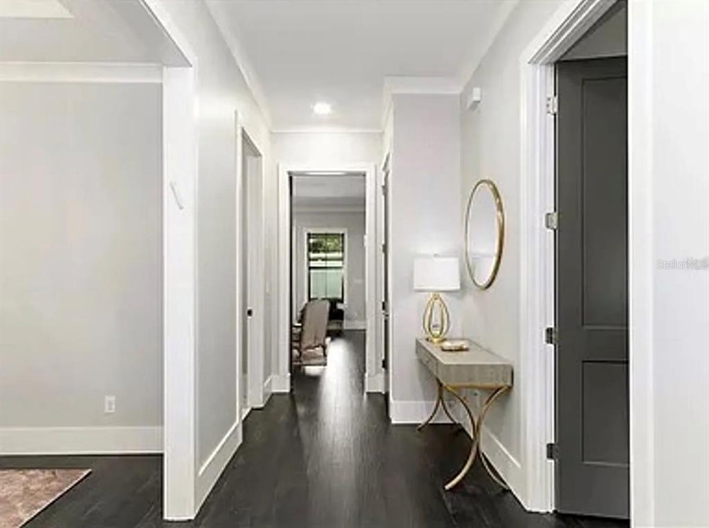 A hallway with dark wood flooring leads to a room with a chair and window — 2234 HOWARD DRIVE, WINTER PARK, FL
