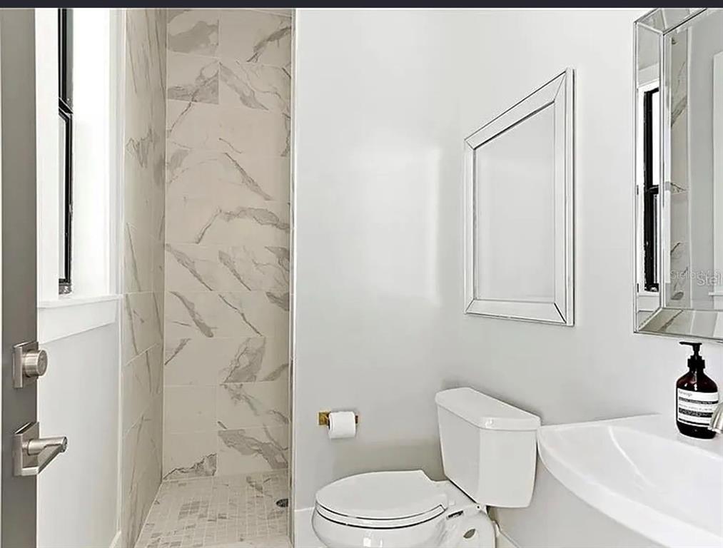 A modern bathroom features a walk-in shower with marble-look tile, a toilet, and a vanity — 2234 HOWARD DRIVE, WINTER PARK, FL