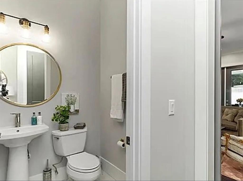A small bathroom features a pedestal sink, a round gold-framed mirror, and a white toilet — 2234 HOWARD DRIVE, WINTER PARK, FL