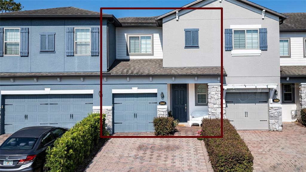 A two-story townhouse exterior features a blue garage door, stone accents, and a paved driveway — 2840 WHITE ISLE LN, ORLANDO, FL