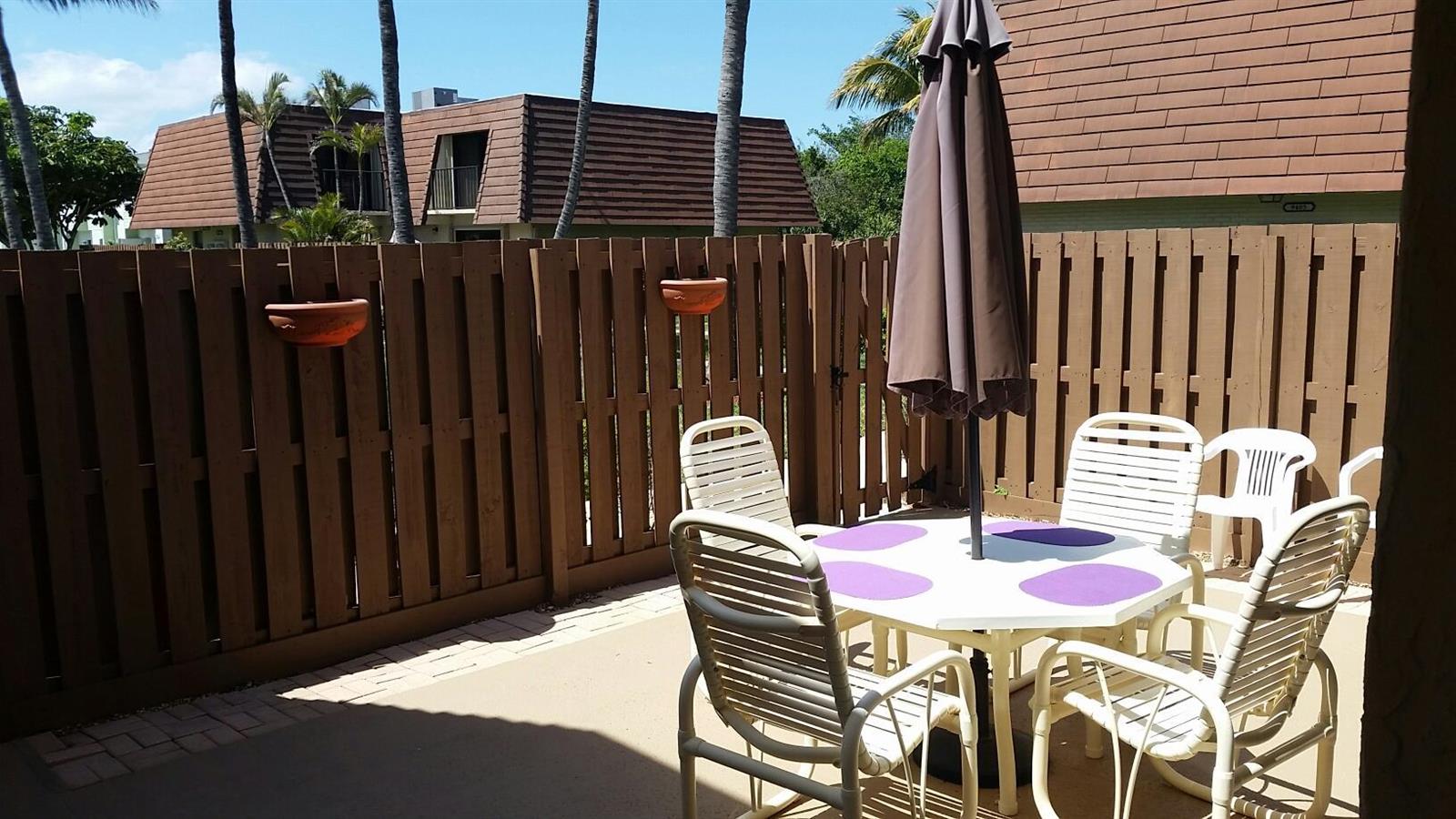 A patio with a white table, chairs, a closed umbrella, and a wooden privacy fence — 9403 S Ocean Drive # 3d, Jensen Beach FL 34957, JENSEN BEACH, FL