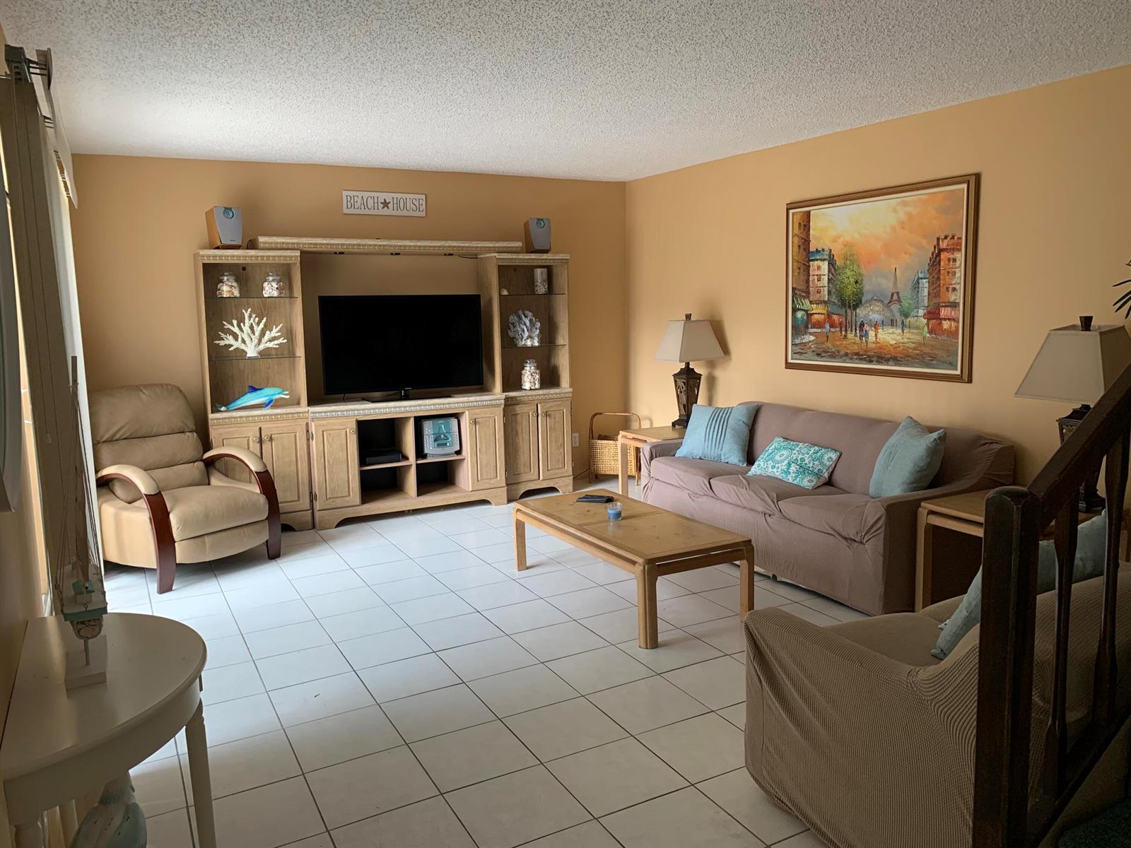 A living room with beige walls, tile flooring, a large entertainment center, and a sofa — 9403 S Ocean Drive # 3d, Jensen Beach FL 34957, JENSEN BEACH, FL