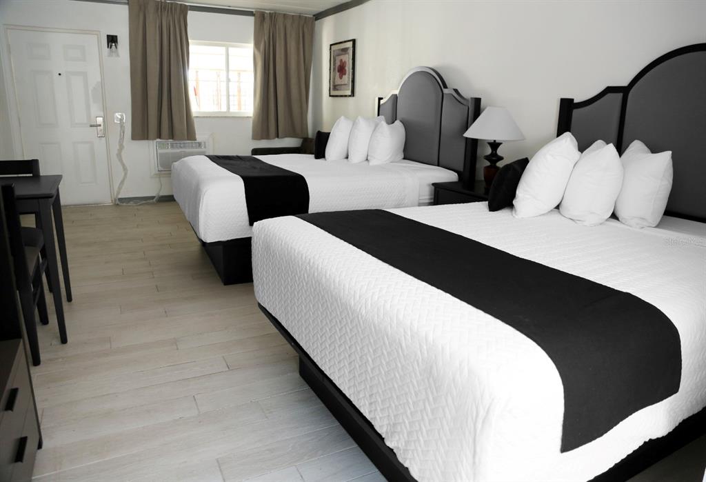 A hotel room features two queen beds with white linens, black runners, and grey headboards — 14711 GULF BOULEVARD, MADEIRA BEACH, FL