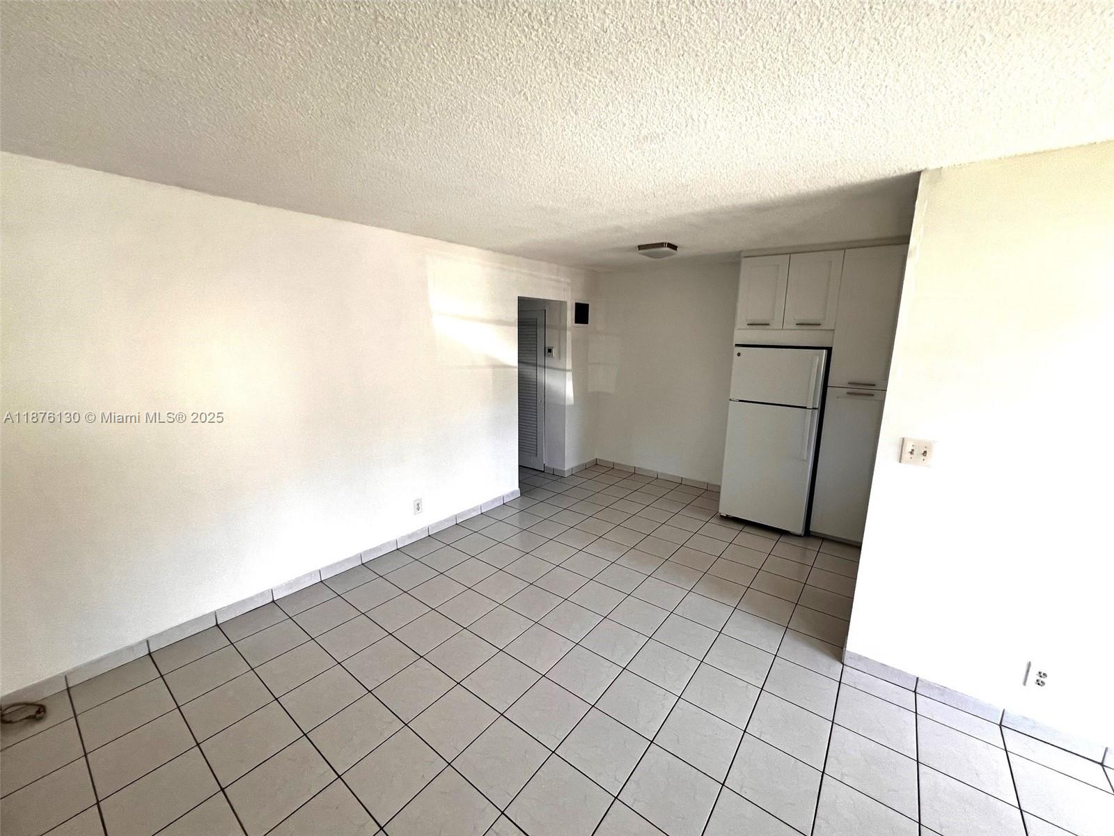 A room with white walls, light-colored floor tiles, and a white refrigerator — 2145 Pierce St # 105, Hollywood FL 33020, HOLLYWOOD, FL