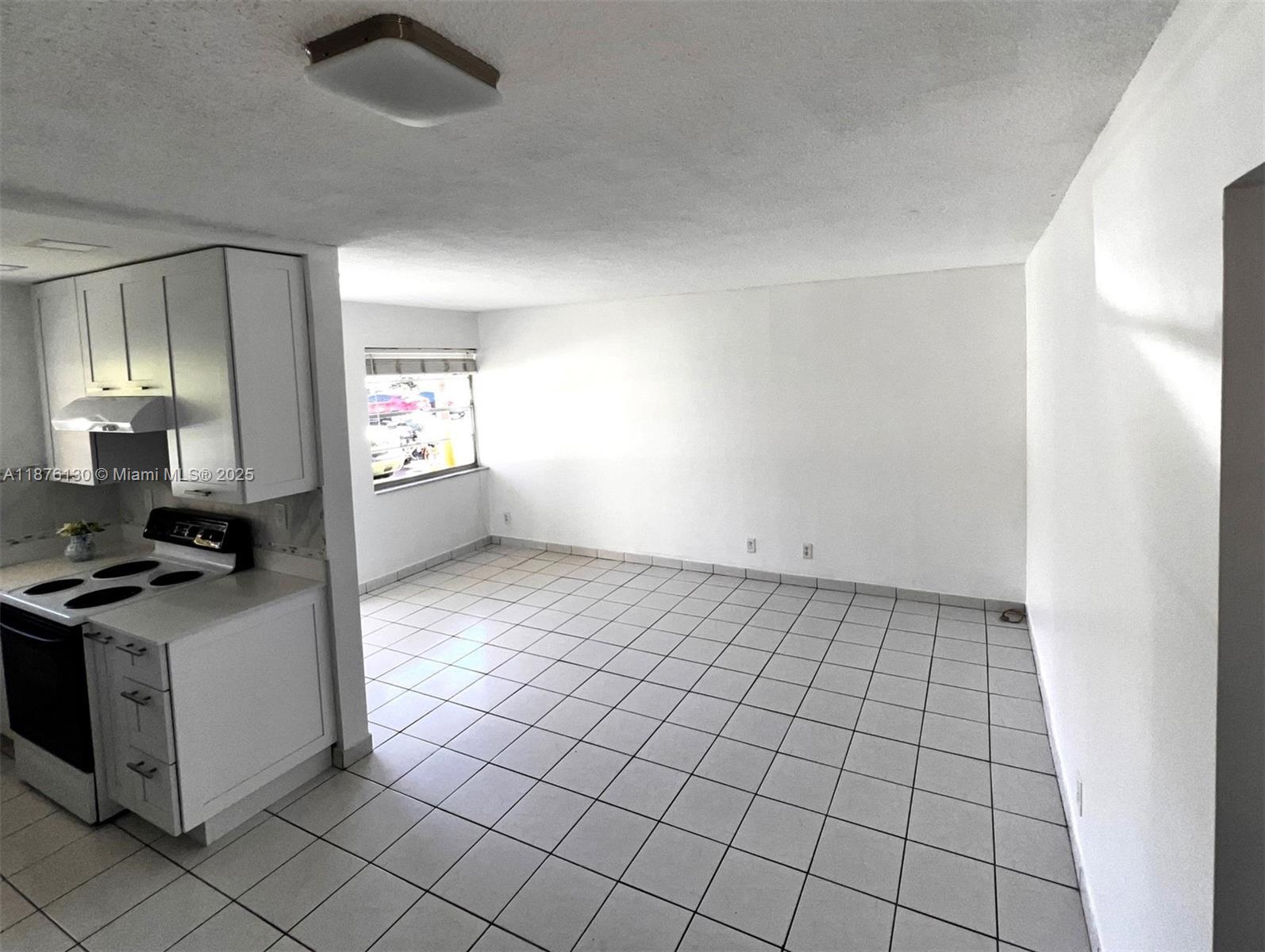 A kitchen with white cabinets and a stove opens into a tiled living area — 2145 Pierce St # 105, Hollywood FL 33020, HOLLYWOOD, FL