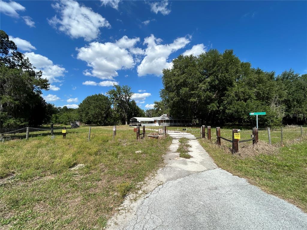 A gravel driveway leads to a house behind a fenced yard with large trees — 5618 CO RD 44A ROAD, WILDWOOD, FL