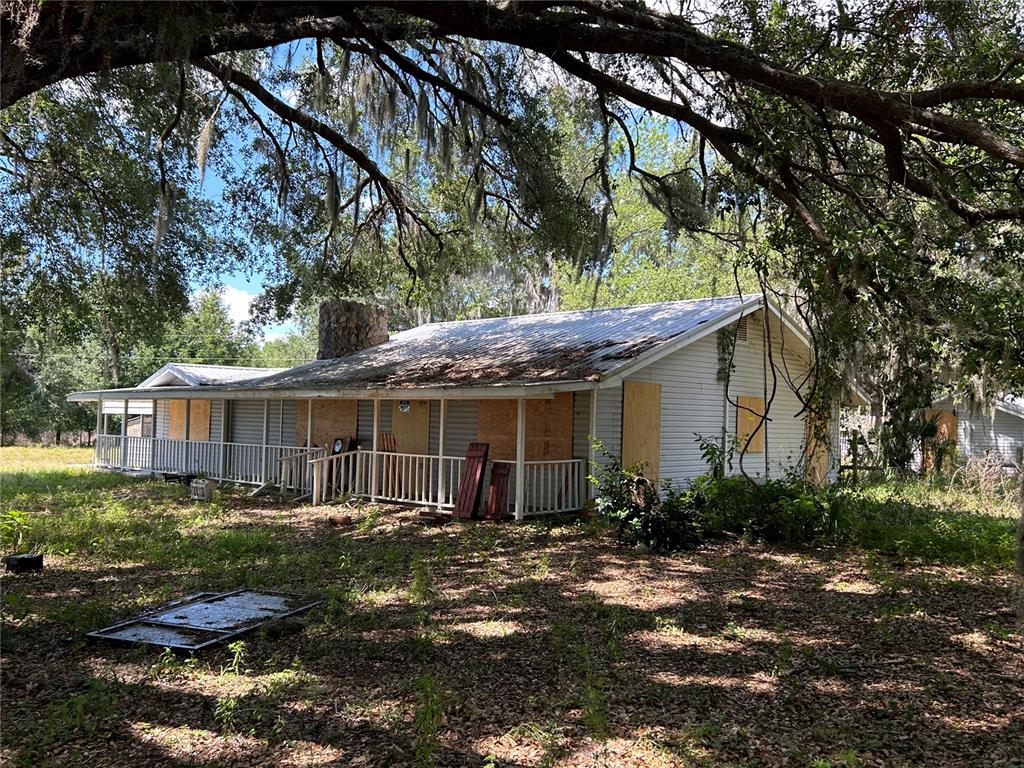 A single-story house with a metal roof and boarded-up windows sits under large oak trees — 5618 CO RD 44A ROAD, WILDWOOD, FL
