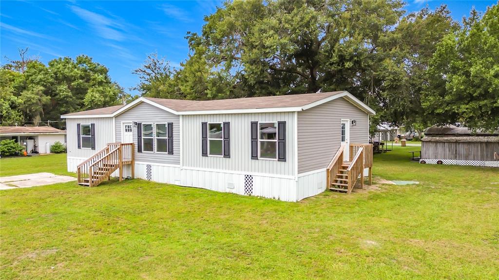 A light gray manufactured home with dark shutters and two wooden entry staircases on grass — 1626 TARPON BOULEVARD, ST CLOUD, FL