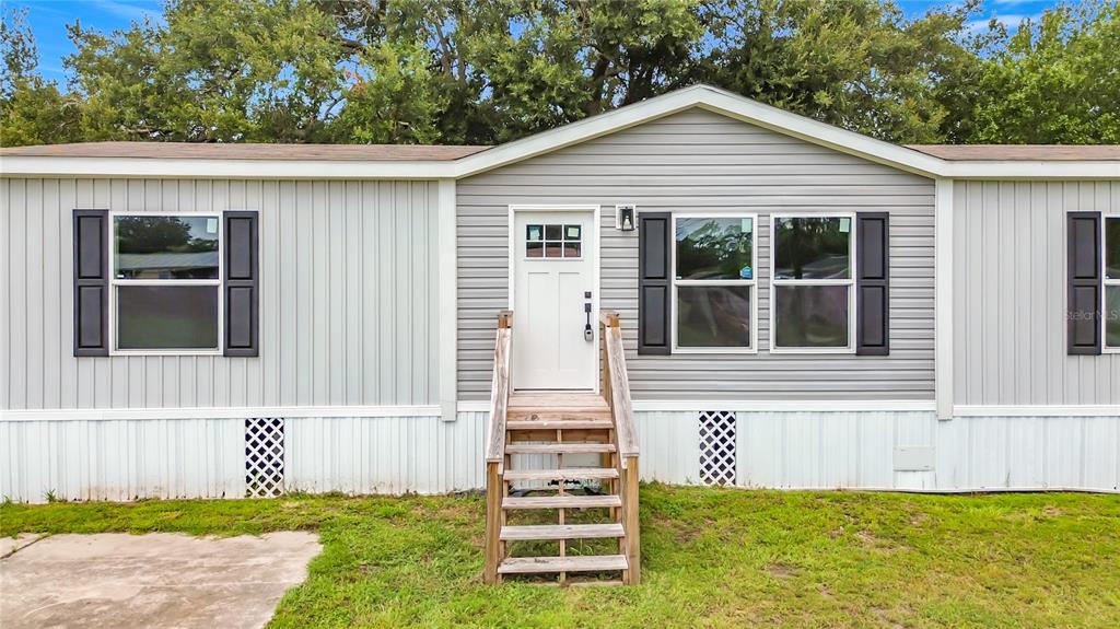A single-story manufactured home with grey horizontal siding, black shutters, and wooden front steps — 1626 TARPON BOULEVARD, ST CLOUD, FL