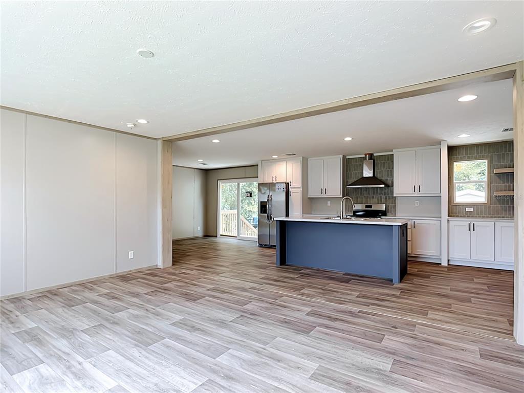An open-concept kitchen and living area features wood-look flooring, white cabinetry, and a blue island — 1626 TARPON BOULEVARD, ST CLOUD, FL