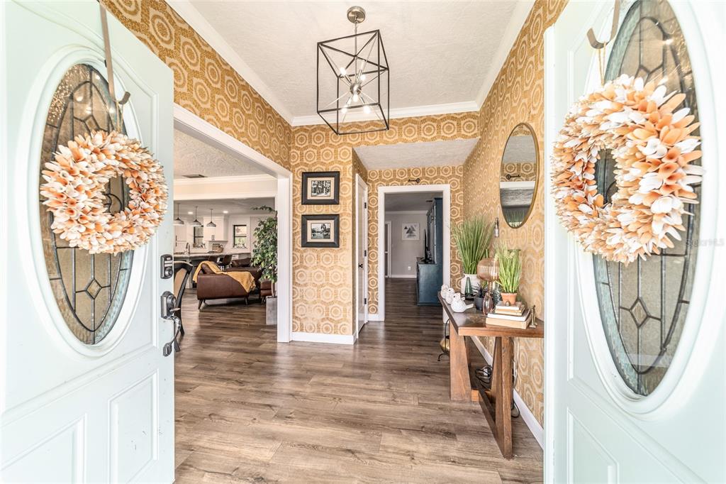 An entryway with patterned gold wallpaper, wood-look flooring, and a modern geometric light fixture — 1308 SE 18TH STREET, OCALA, FL
