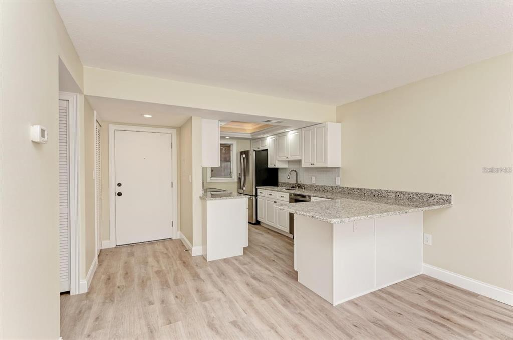 A kitchen with white cabinets, granite countertops, and light wood-look flooring — 129 TYLER DRIVE UNIT 101, SARASOTA, FL