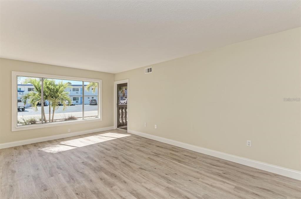 An empty room with light-colored walls, wood-look flooring, a large window, and a door — 129 TYLER DRIVE UNIT 101, SARASOTA, FL
