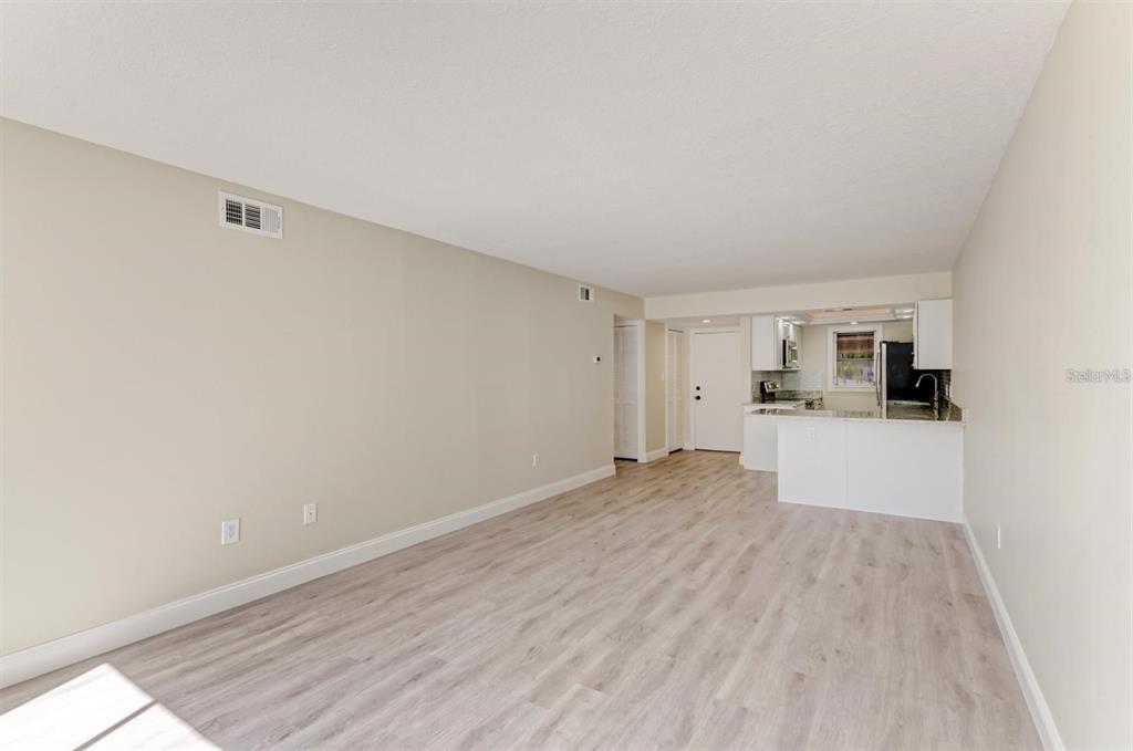 A living room with light wood-look flooring leads to an open kitchen with white cabinets — 129 TYLER DRIVE UNIT 101, SARASOTA, FL