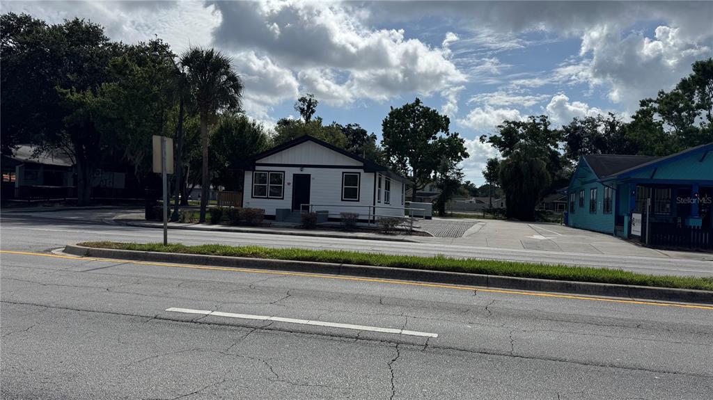 A white house with a black roof sits next to a blue building along a road — 1121 N MAIN STREET, KISSIMMEE, FL