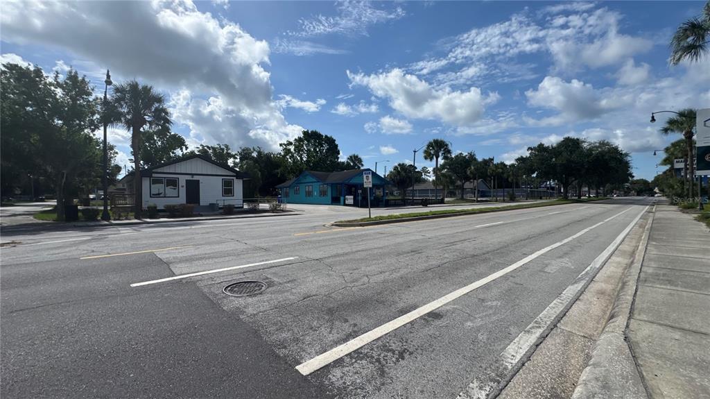 A street-level view shows a paved road leading toward two commercial buildings under a blue sky — 1121 N MAIN STREET, KISSIMMEE, FL
