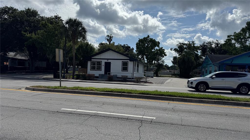 A white, single-story building with a black roof sits near a road with a car — 1121 N MAIN STREET, KISSIMMEE, FL