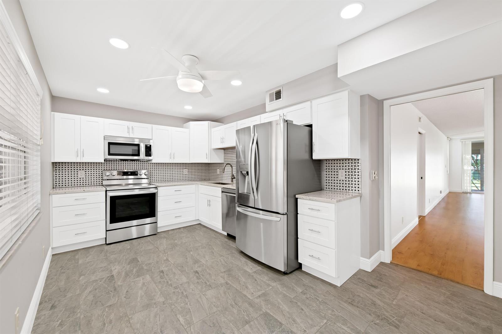 A kitchen features white cabinetry, stainless steel appliances, a tiled backsplash, and gray flooring — 800 Cypress Grove Drive # 211, Pompano Beach FL 33069, POMPANO BEACH, FL