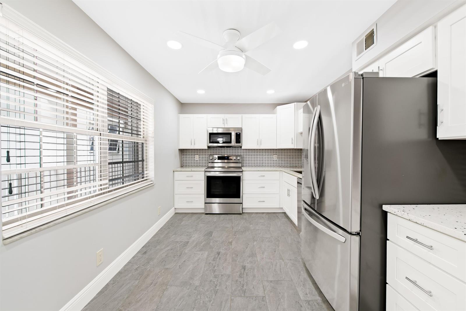 A kitchen features white cabinets, stainless steel appliances, a tiled backsplash, and gray flooring — 800 Cypress Grove Drive # 211, Pompano Beach FL 33069, POMPANO BEACH, FL