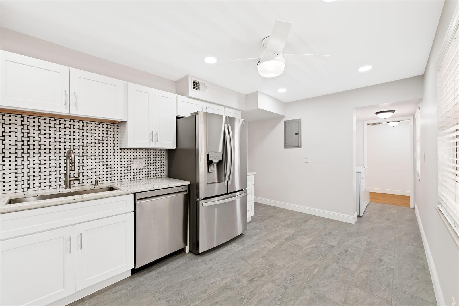 A kitchen features white cabinets, stainless steel appliances, a patterned backsplash, and gray tile flooring — 800 Cypress Grove Drive # 211, Pompano Beach FL 33069, POMPANO BEACH, FL