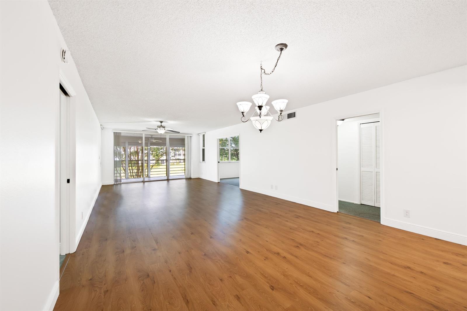An empty living room features wood-look flooring, white walls, a chandelier, and a sliding door — 800 Cypress Grove Drive # 211, Pompano Beach FL 33069, POMPANO BEACH, FL