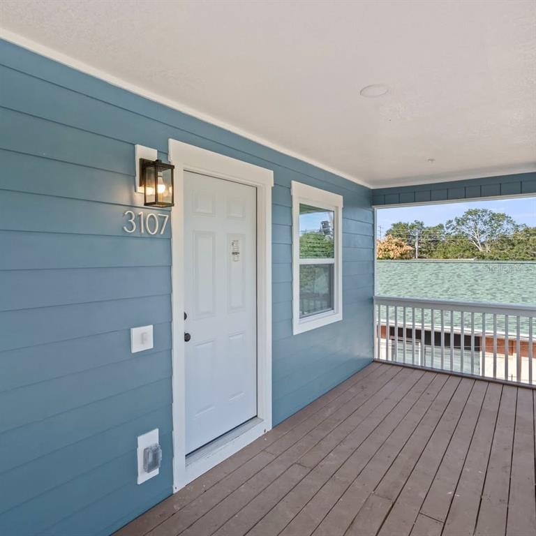 A blue-sided porch features a white door, a wall-mounted light, and a wooden deck — 3107 16TH STREET N, ST PETERSBURG, FL