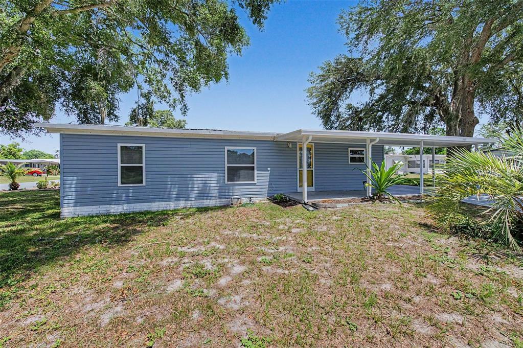 A blue single-story house with a covered porch and a yard with large trees — 7338 FIRST LOOP AVENUE, BROOKSVILLE, FL
