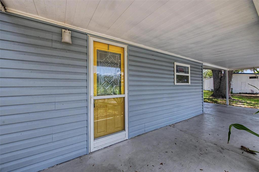 A blue-sided home exterior features a yellow storm door and a covered concrete porch — 7338 FIRST LOOP AVENUE, BROOKSVILLE, FL
